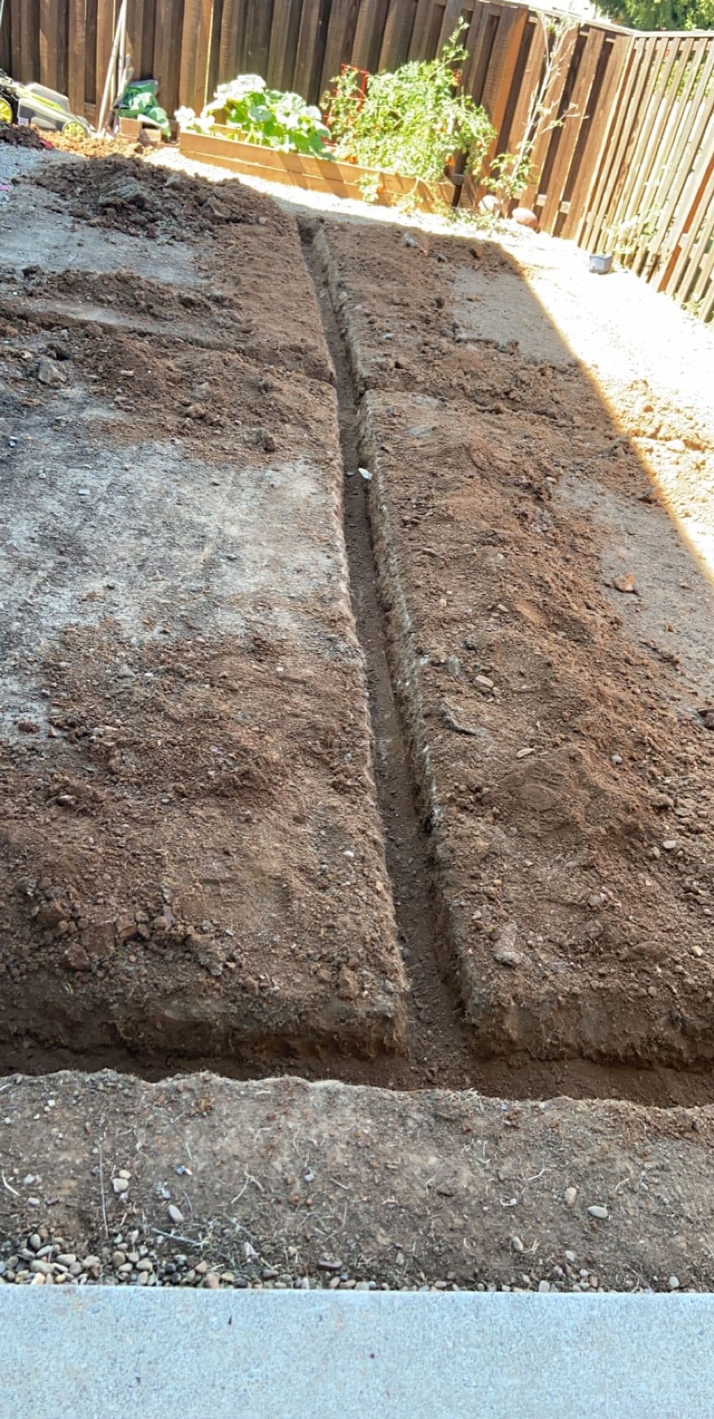 Excavated backyard area showing parallel trenches in dry soil, ready for landscaping.