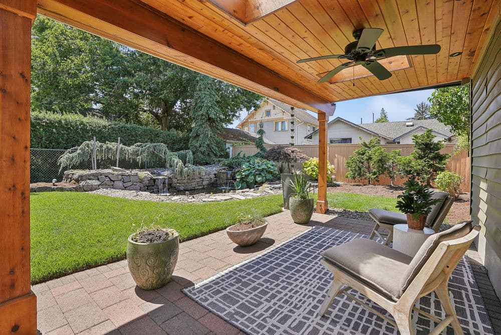 Cozy patio area with seating, potted plants, and pond view in a lush backyard.