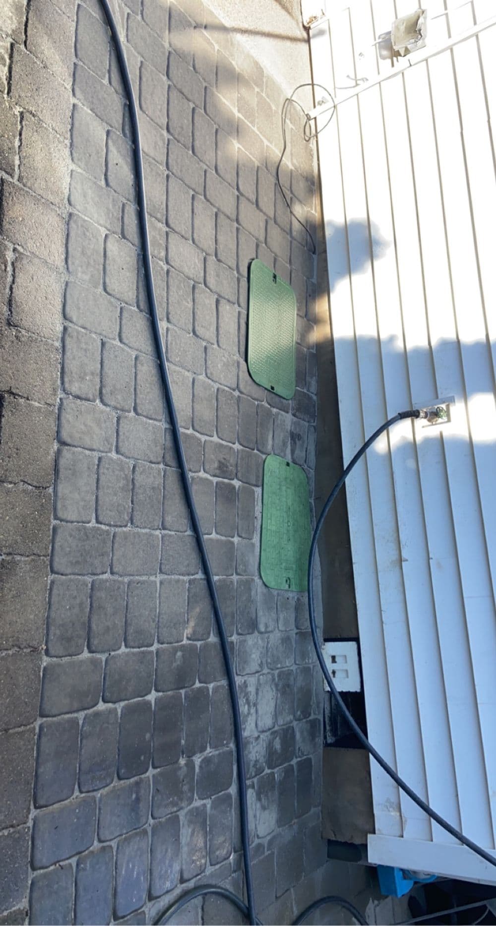 Green mats on a cobblestone patio with electrical cables and a nearby building wall.