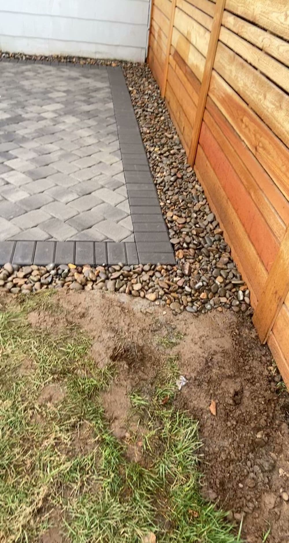 Patio area with pavers, gravel edge, and wooden fence in a residential yard.