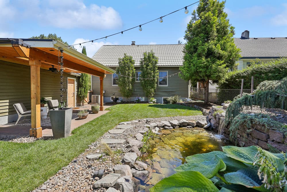 Lush backyard with pond, decorative stones, and string lights illuminating a cozy patio.