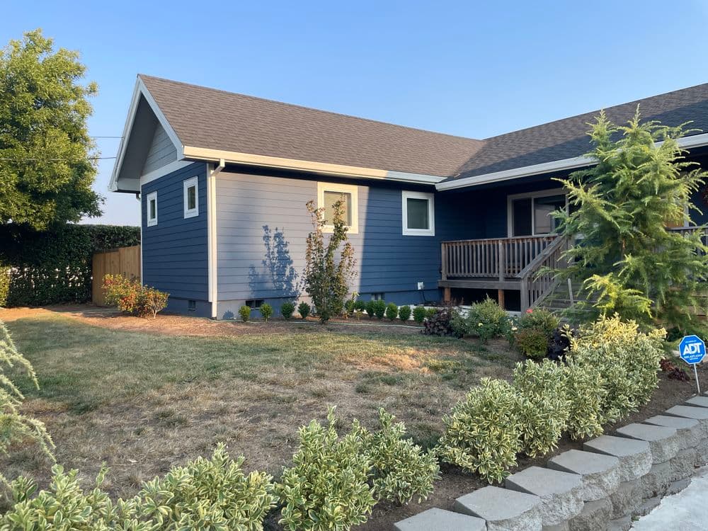 Blue house exterior with garden and porch in a sunny neighborhood setting.