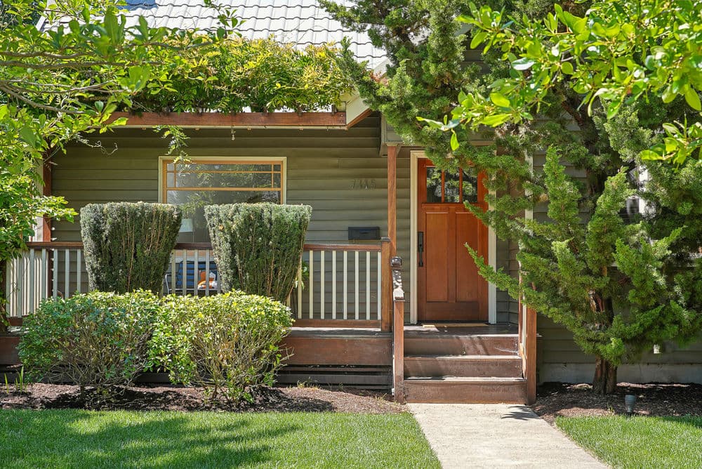 Charming green house exterior with lush landscaping and inviting wooden front door.