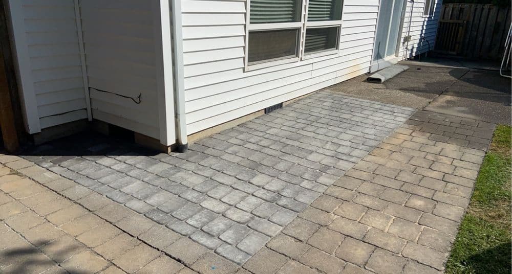 Paved patio area with gray stone tiles beside a white house exterior.