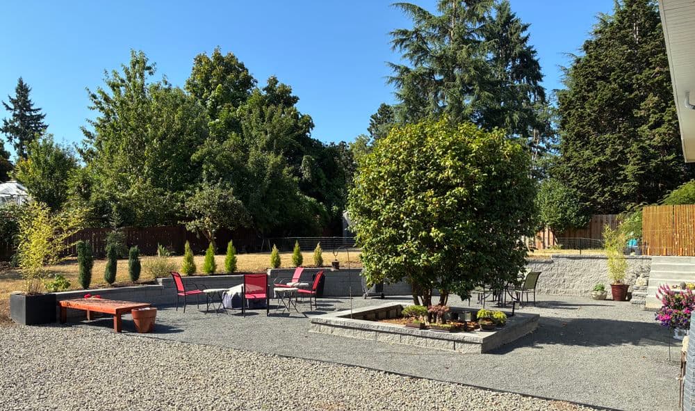 Modern outdoor patio with seating, landscaped garden, and trees under clear blue sky.