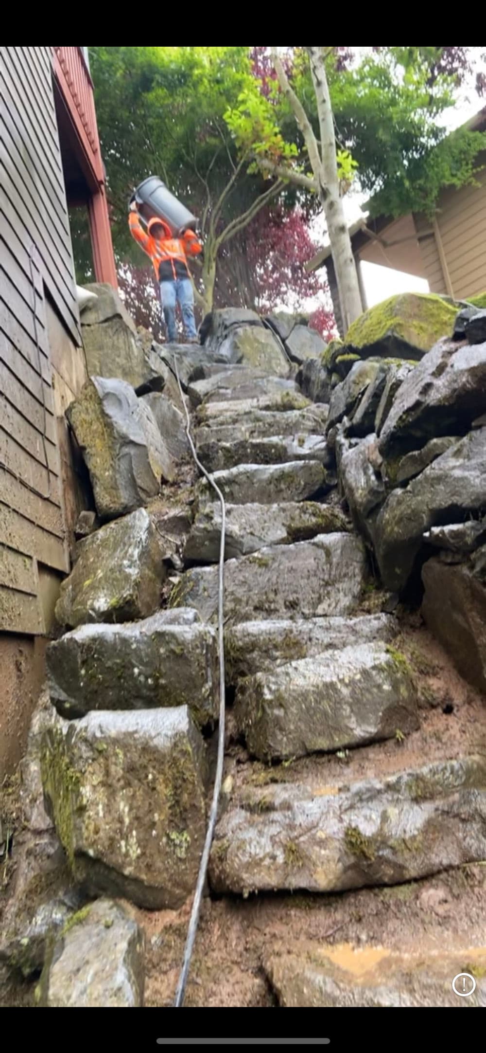 Worker in safety gear climbing stone steps carrying a bucket during landscaping project.