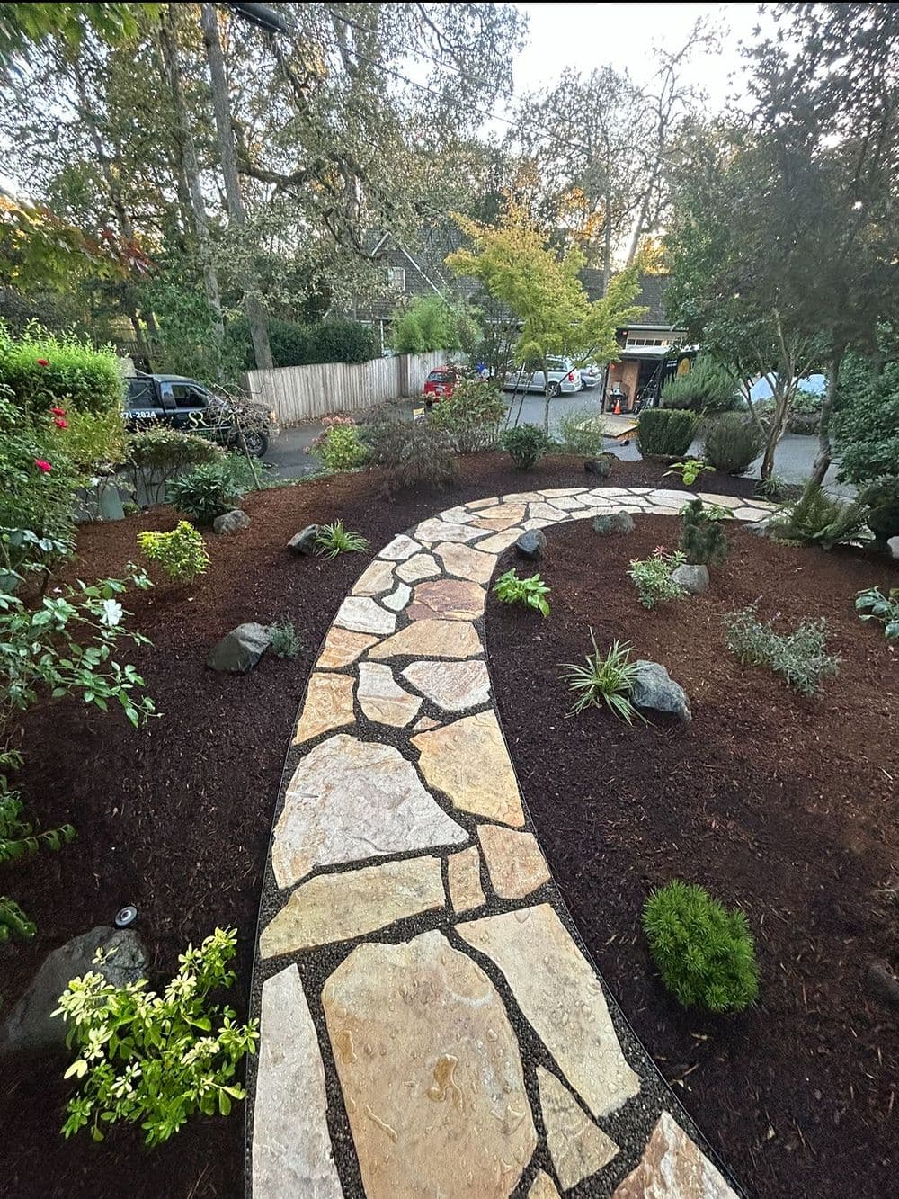 Curved stone pathway through landscaped garden with plants and rocks, inviting outdoor space.