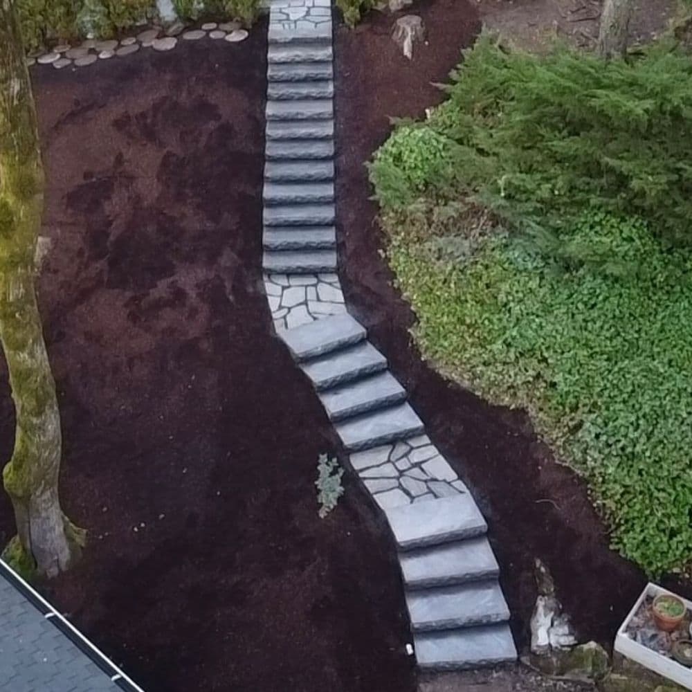 Winding stone pathway through landscaped garden with lush greenery and mulch.