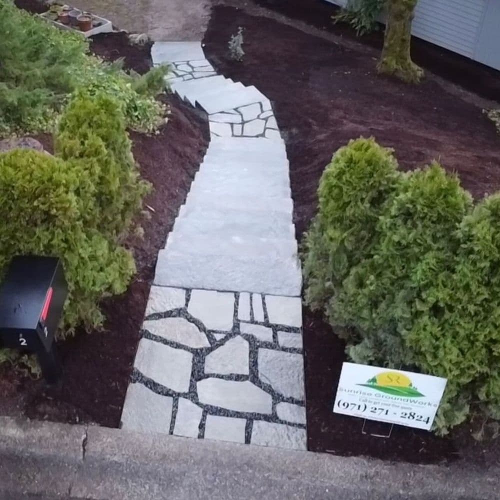 Curved stone pathway framed by shrubs with landscaping sign displaying contact info.