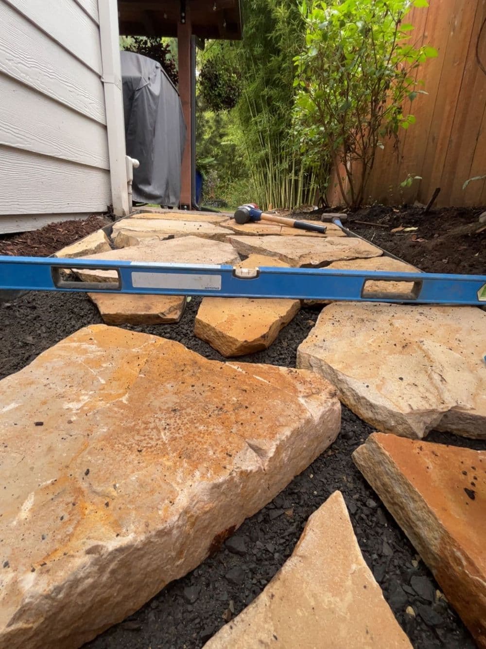 Stone pathway under construction with a level tool and landscaping elements.